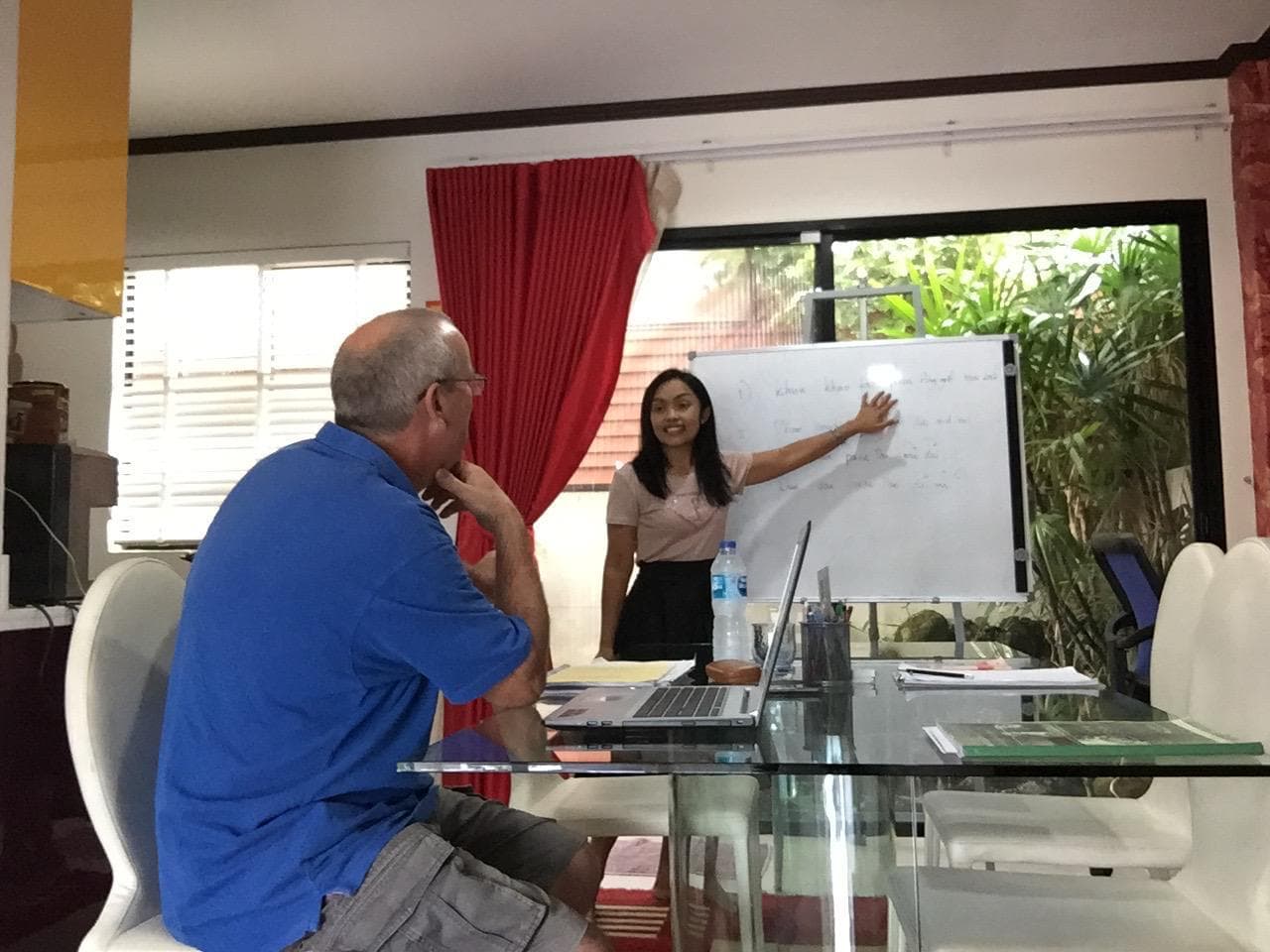 Kru Jittra explaining pronunciation and tones at the whiteboard with a student